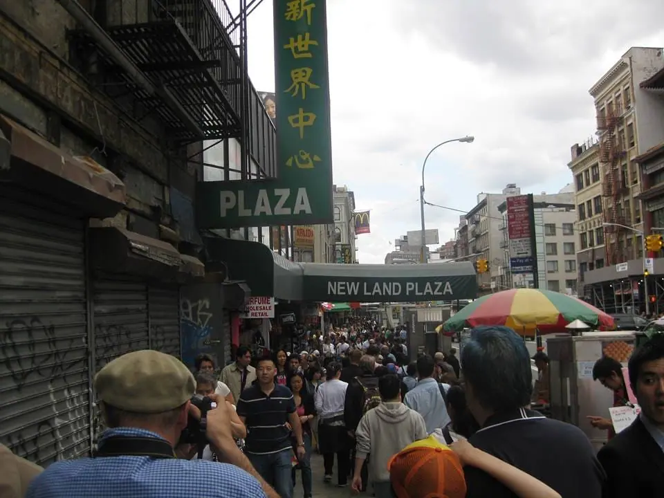 Una calle de Chinatown llena de gente, bajo el cartel New Land Plaza